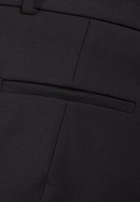 Pantalon en tissu noir avec une texture lisse, une coupe slim et une seule poche arrière à ouverture horizontale.