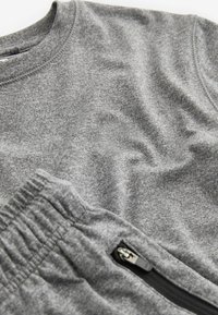 Grijze sporttop en -broek gemaakt van een zachte katoenmengsel; voorzien van een elastische tailleband en een ritszak op de broek.