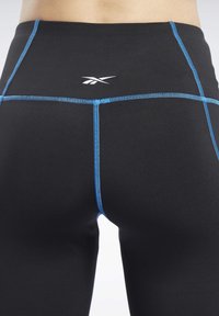 Černé legíny s modrými švy, se znakem výrazně umístěným. Hladký povrch a přiléhavý design vhodný pro aktivní nošení.