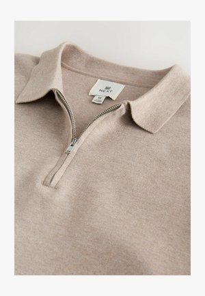Svijetlosmeđi polo s patentnim zatvaračem, prilagođenim ovratnikom i mekim pletenim teksturom. Oznaka označava "NEXT," veličina M. Jednostavan i čisti dizajn.