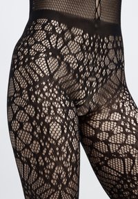 Meias de rede pretas com um padrão texturizado semelhante a rendas, apresentando formas variadas e áreas abertas, cintura elástica para um ajuste seguro.