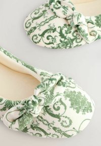 Rohelise ja valge mustriga flanellist sussid, millel on ees sõlme detail, ümar varvas ja pehme sisekate.