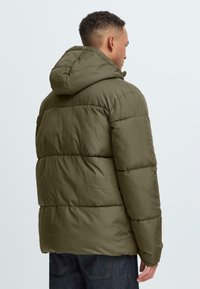 Oliven grønn hettejakke med pufferdesign og quiltede seksjoner, laget av et glatt materiale. Har en løs passform med elastiske mansjetter og kant.