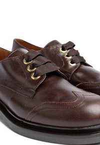 Bruine leren schoenen met een gladde textuur, ontworpen met een ronde neus, gouden vetergaatjes en bruine lintveters. Voorzien van decoratieve stiksels.