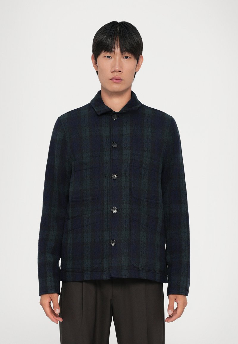 Giacca di lana a quadri blu navy e verde con chiusura a bottoni, colletto da camicia e due tasche frontali. Texture morbida e design strutturato.