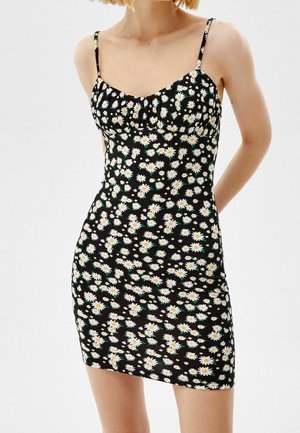 Robe mini noire avec imprimé marguerite blanche, bretelles spaghetti, corsage froncé et design ajusté avec une texture lisse.