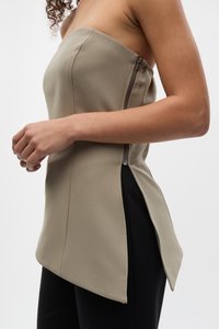 Beige trägerloses Oberteil mit geradem Ausschnitt, seitlichem Reißverschluss und geschwungener Säume. Kombiniert mit schwarzen, engen Hosen, die eine glatte Textur haben.