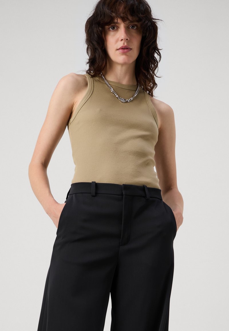 Getailleerde, ribbelige tanktop in kaki, gecombineerd met hoge, wijde zwarte broeken. Gevuld met een eenvoudige zilveren ketting.