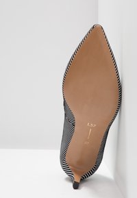 Chaussure à talon haut à bout pointu, rayée noir et blanc, vue de profil sole, taille 37 avec un talon aiguille fin.