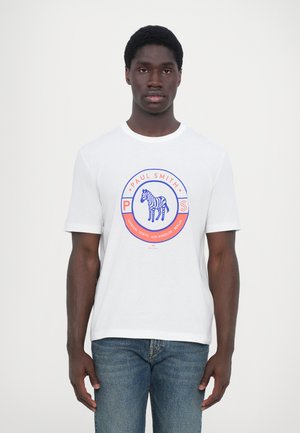 White cotton t-shirt featuring a circular graphic with a blue zebra, red accents, and "Paul Smith" text, paired with blue denim jeans.