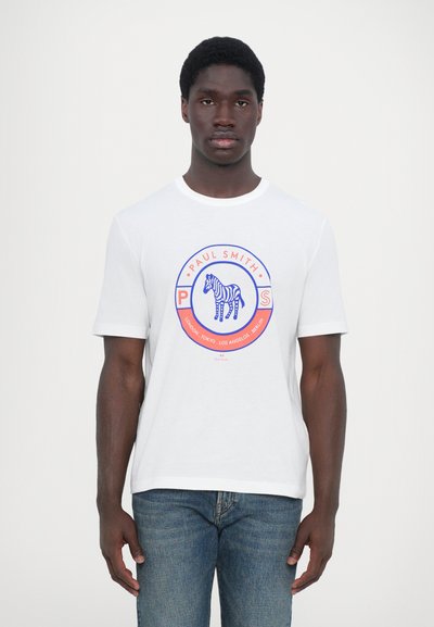 Fehér pamut póló, kerek grafikával, kék zebrával, piros kiegészítőkkel és "Paul Smith" felirattal, kék farmernadrággal párosítva.