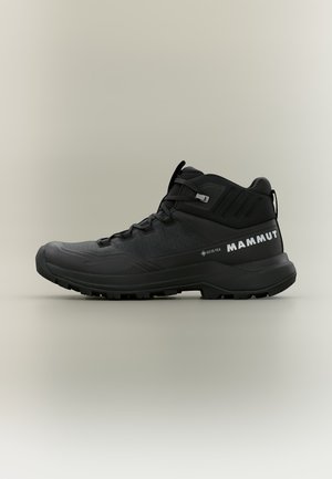Zwarte mid-hoge wandelschoen met robuuste zool, veters, Gore-Tex label en wit Mammut-logo op de hiel.
