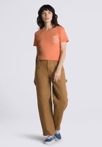 Short-sleeve, orange t-shirt with white Vans logo, paired with loose, tan cargo pants and blue sneakers. Simple design, relaxed fit.