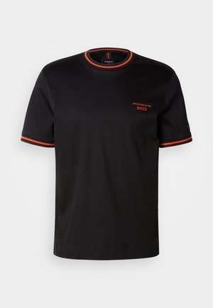 Fekete pamut póló rövid ujjakkal, piros díszítéssel a nyakvonalon és az ujjakon, valamint piros hímzett logóval az elején.