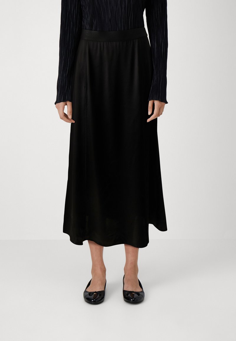 Svart sateng midi-skjørt med en glatt tekstur og en tettsittende midje, paret med svarte ballettleiligheter, som viser minimal detaljering.