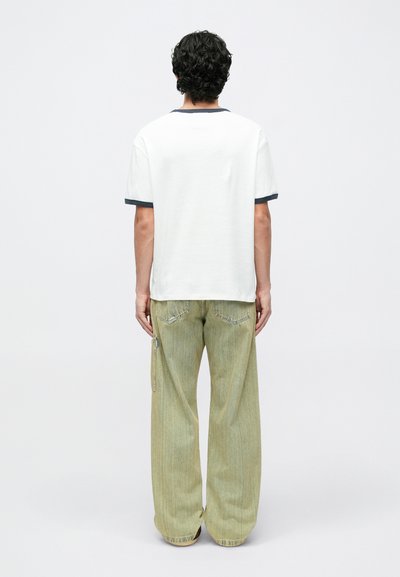 Fehér póló tengerészkék gallérral és ujjakkal, világoszöld, széles szárú farmerral, oldalsó cipzárral és varrott részletekkel párosítva.