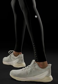 Czarne legginsy kompresyjne z odblaskowym logo i kropkowymi akcentami. Szare buty sportowe mają siateczkową cholewkę i wyściełaną podeszwę dla lepszej podpory.