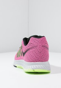 Scarpa da corsa rosa e nera con accenti verdi, suola bianca, vista dal retro su sfondo bianco uniforme.