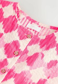 Chemise à col rond à motifs roses et blancs avec trois boutons en forme de fleurs et une étiquette "NEXT Made in India".