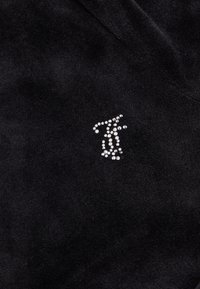 Un tessuto nero con una morbida texture presenta un logo argentato scintillante realizzato con strass, aggiungendo un dettaglio riflettente all'intero design.