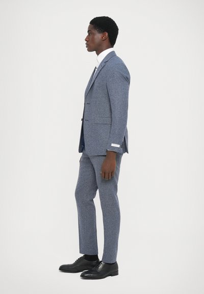 Tailored blue tweed suit with a slim fit, single-breasted jacket, matching trousers, and black leather shoes. Crisp white shirt underneath.