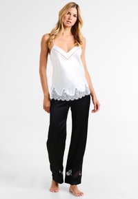 White satin camisole with lace trim, featuring a V-neck and adjustable straps, paired with black satin pants with lace accents at the hem.