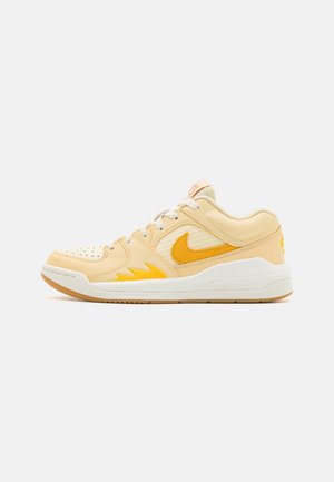 Zapatillas de deporte en cuero amarillo claro, con un destacado logo en forma de swoosh amarillo, cuello acolchado y suela de goma con acentos amarillos.