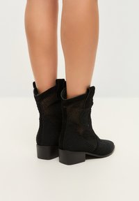Botas negras hasta el tobillo con parte superior de malla y acentos de ante. Los tacones block y el diseño de punta redondeada proporcionan una silueta estructurada.