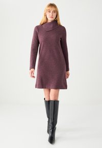 Robe en maille bordeaux à manches longues avec un col montant et une coupe décontractée, associée à des bottes en cuir noir arrivant aux genoux avec une texture lisse.