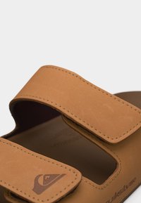 Ταμπά σανδάλι με δύο ρυθμιζόμενους ιμάντες, με ορατή ραφή και λογότυπο στον μπροστινό ιμάντα.