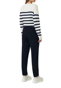 Sweter w paski w kolorze granatowym i białym o luźnym kroju, zestawiony z granatowymi spodniami. Model nosi jasne trampki. Miękka dzianinowa faktura.