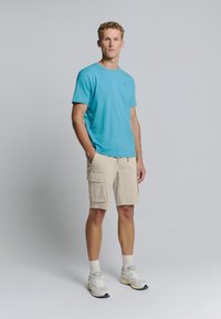 Lichtblauwe t-shirt met korte mouwen, beige cargoshorts met zijzakken, grijze sneakers. Casual fit met een eenvoudig ontwerp en een zachte textuur.