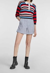 Rood, blauw en wit gestreepte gebreide trui met een kraag, gecombineerd met hoge, blauw en wit gestreepte shorts. Zwarte enkellaarsjes.