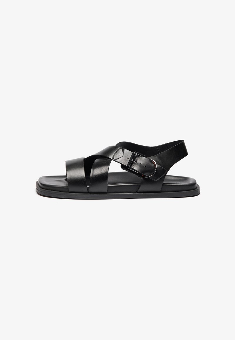 Sandales en cuir noir avec des brides croisées, une boucle à l'arrière, une semelle basse et une finition lisse pour la durabilité et le confort.