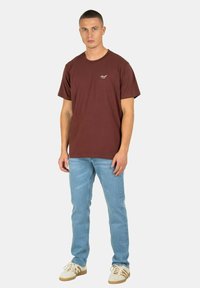 Camiseta de algodón marrón de manga corta y cuello redondo, combinada con vaqueros azules y zapatillas beige con cordones blancos y acentos claros.