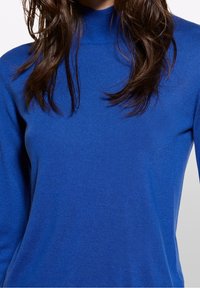 Blå långärmad polotröja i ett texturerat stickat tyg. Har en smal passform med en mjuk och slät yta samt minimal sömnad.