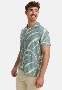 Short-sleeve shirt in light blue fabric with white leaf patterns, featuring a collar and button closure, suitable for casual wear.