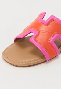 Slide sandal made of orange leather with a large pink zigzag strap. Brown footbed with stitching detail, smooth texture, and open toe design.