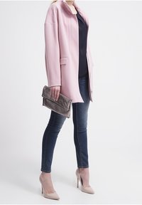 Light pink blazer with a collar, paired with a navy top, dark denim jeans, cream high heels, and a gray clutch bag. Smooth texture and tailored fit.