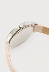 Hopeinen kello, jossa on pyöreä kruunu ja vaalea vaaleanpunainen nahkahihna, esitetty sivusta valkoista taustaa vasten.