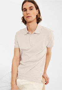 Lichtbeige polo shirt met een kraag, korte mouwen en een gestroomlijnd ontwerp. Kenmerkt zich door een subtiele textuur en een knoopsluiting met twee knopen.