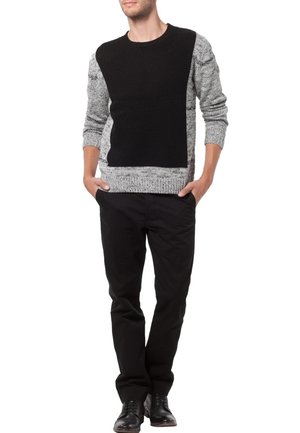 Černý a šedý pletený svetr s texturovaným vzorem, s jednobarevnou černou přední částí a žebrovanými manžetami. Kombinován s černými kalhotami.