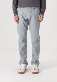 Lyseblå, rette jeans med frontlommer og glidelås, kombinert med hvite sneakers med brune gummisåler.