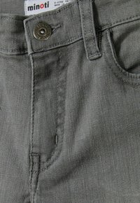 Sive jeans hlače z teksturiranim zaključkom, ki imajo kovinsko gumb, šivane žepe in oznako, ki označuje velikost in blagovno znamko.
