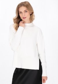 Witte gebreide trui met een hoge hals, lange mouwen en een licht losse pasvorm. Geribbelde details bij de mouwen en de zoom; gladde textuur.
