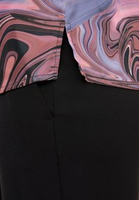 Bunt gemustertes, wirbelndes Gewebe in verschiedenen Rosa-, Lila- und Schwarztönen, übereinandergelegt auf einer glatten schwarzen Hose. Sichtbare Nähdetails.