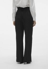 Svarta randiga byxor med hög midja, utrustade med två bakfickor, vida ben och en slät textur, parat med en vit skjorta.