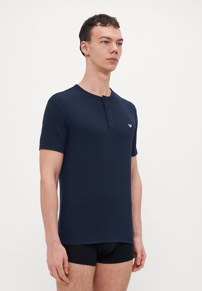 T-shirt henley à manches courtes côtelé bleu marine avec trois boutons, comportant un petit logo sur la poitrine gauche et un col rond.