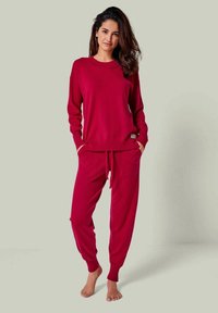 Rotes Loungewear-Set mit einem langärmligen Oberteil mit geripptem Kragen und passenden Jogginghosen mit elastischem Bund und seitlichen Taschen.