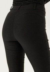 Zwarte rekbare legging met een gladde textuur, aansluitend ontwerp en subtiele naaddetails op de achterkant. Eenvoudige tailleband zonder versieringen.